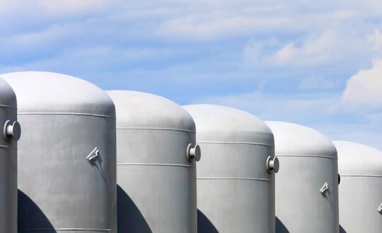 Row of industrial silos against a blue sky with clouds, storage tanks for agricultural or chemical use, metal containers for bulk storage, commercial farming infrastructure