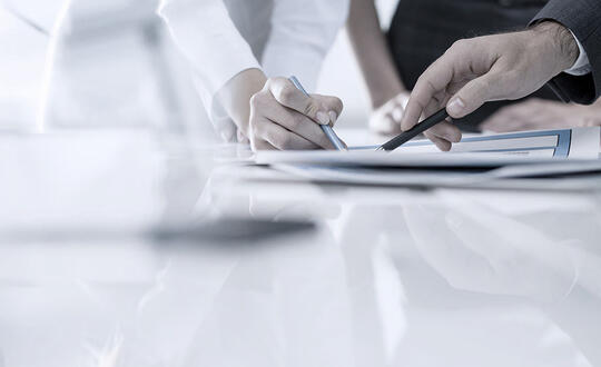 Business professionals reviewing documents at a meeting in a modern office setting, focussing on paperwork with pen in hand for collaborative analysis.