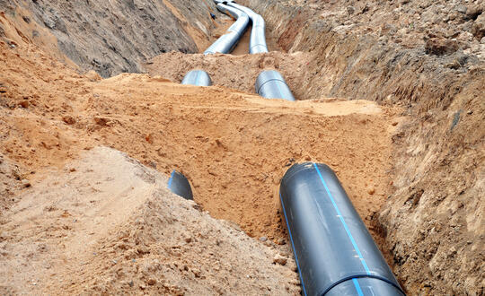 Large water pipes being laid in a trench during infrastructure development works, showcasing construction site for utility services installation in urban setting.