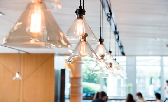 A row of stylish pendant lights with exposed filament bulbs suspended from a ceiling, illuminating a modern interior with warm light, potentially in a chic café or contemporary workspace.