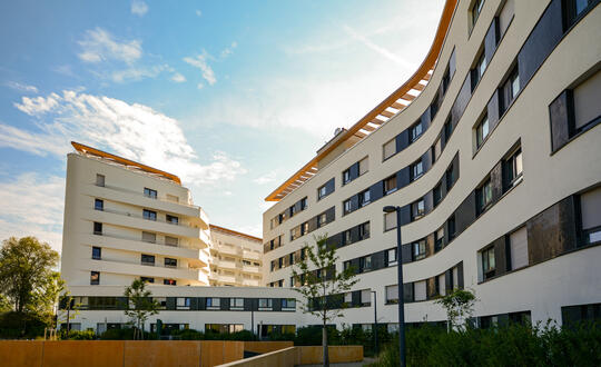 Modern residential architecture with curved white buildings under a clear blue sky in an urban environment.