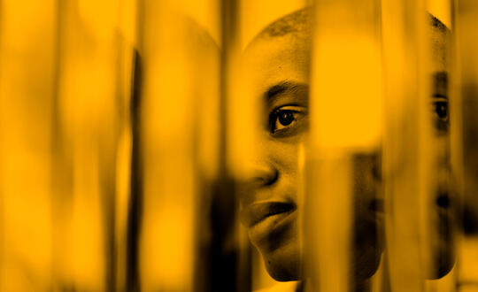 Person looking through gaps in blinds. Photo edited with yellow wash.