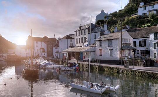 Quaint British seaside village at sunset with waterfront houses, moored boats, and tranquil harbour waters.