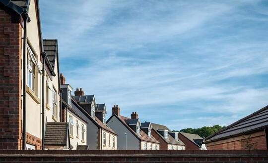 Row of British terraced houses with solar panels on rooftops under blue sky with light cloud coverage