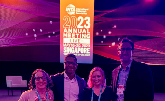 WBD attorneys Marie Anne Mastrovito, Nick Hawkins, Laura Kees, and Pete Bromaghim stand in front of a banner for the International Trademark Association Annual Meeting in Singapore.