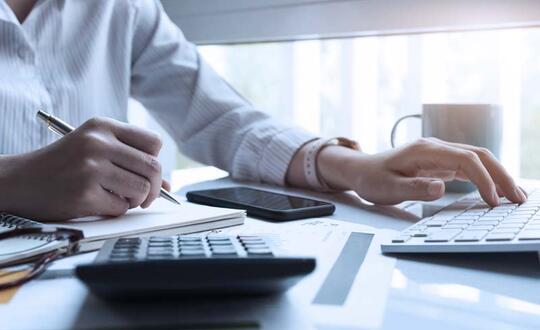 Business professional working on financial report with calculator and computer at a modern office desk.