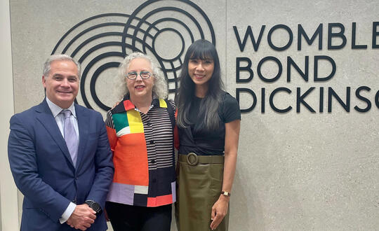 Francisco Balduzzi and Azie Aziz of our Houston office stand with artist Luisa Duarte in front of a Womble Bond Dickinson sign