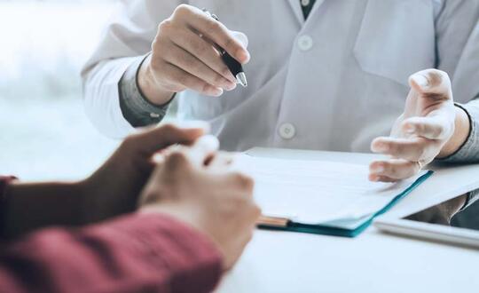 Doctor consulting with patient, healthcare professional explaining diagnosis, medical consultation, close-up of hands with clipboard, GP appointment in clinic.