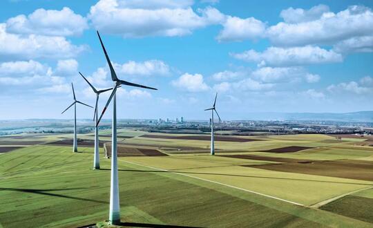 Wind turbines standing in agricultural fields under a blue sky with scattered clouds, illustrating sustainable energy and rural landscape.