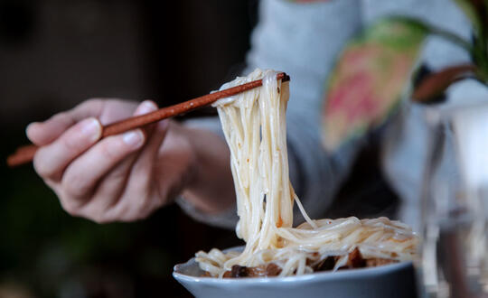 Person using chopsticks to lift steaming noodles from a bowl, exemplifying traditional Asian cuisine.