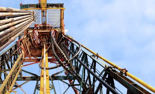 Close-up of offshore oil drilling rig structure with intricate framework and piping against a clear sky.
