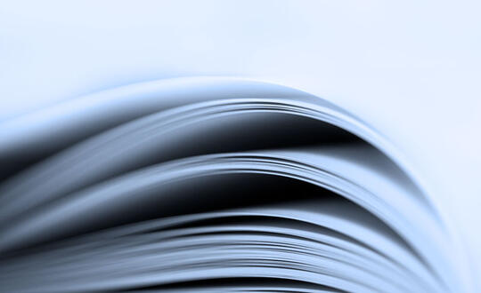 Close-up view of the curved edges of stacked paper sheets, highlighting the texture and layers, with a soft monochromatic blue gradient background.