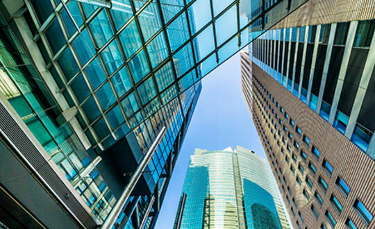 Low angle view of modern skyscrapers with glass facades under a clear blue sky in a bustling city centre, showcasing contemporary urban architecture and commercial real estate development.