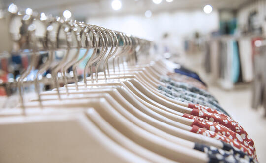 A variety of women's clothing on hangers neatly arranged on a rail in a fashion retail shop, with a focus on floral dresses and blurred background for a shopping ambience.