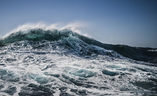 Majestic turquoise wave cresting with frothy white foam in the ocean under a clear blue sky.