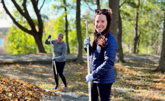 A member of our Boston office pauses from raking leaves and smiles.
