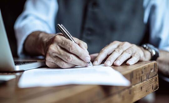 Person signing paper on a wooden table