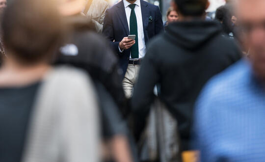 A man checks his phone walking in a crowd of people.